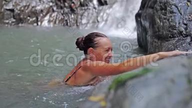 年轻快乐的女人在热带瀑布的池塘里放松游泳。 慢动作。 3840x2160
